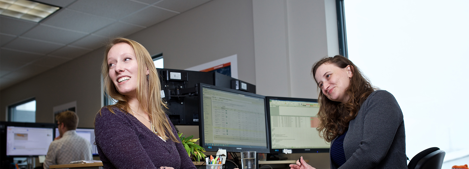 Two employees are sitting near a computer station, smiling at something off to the left not seen in the photo.