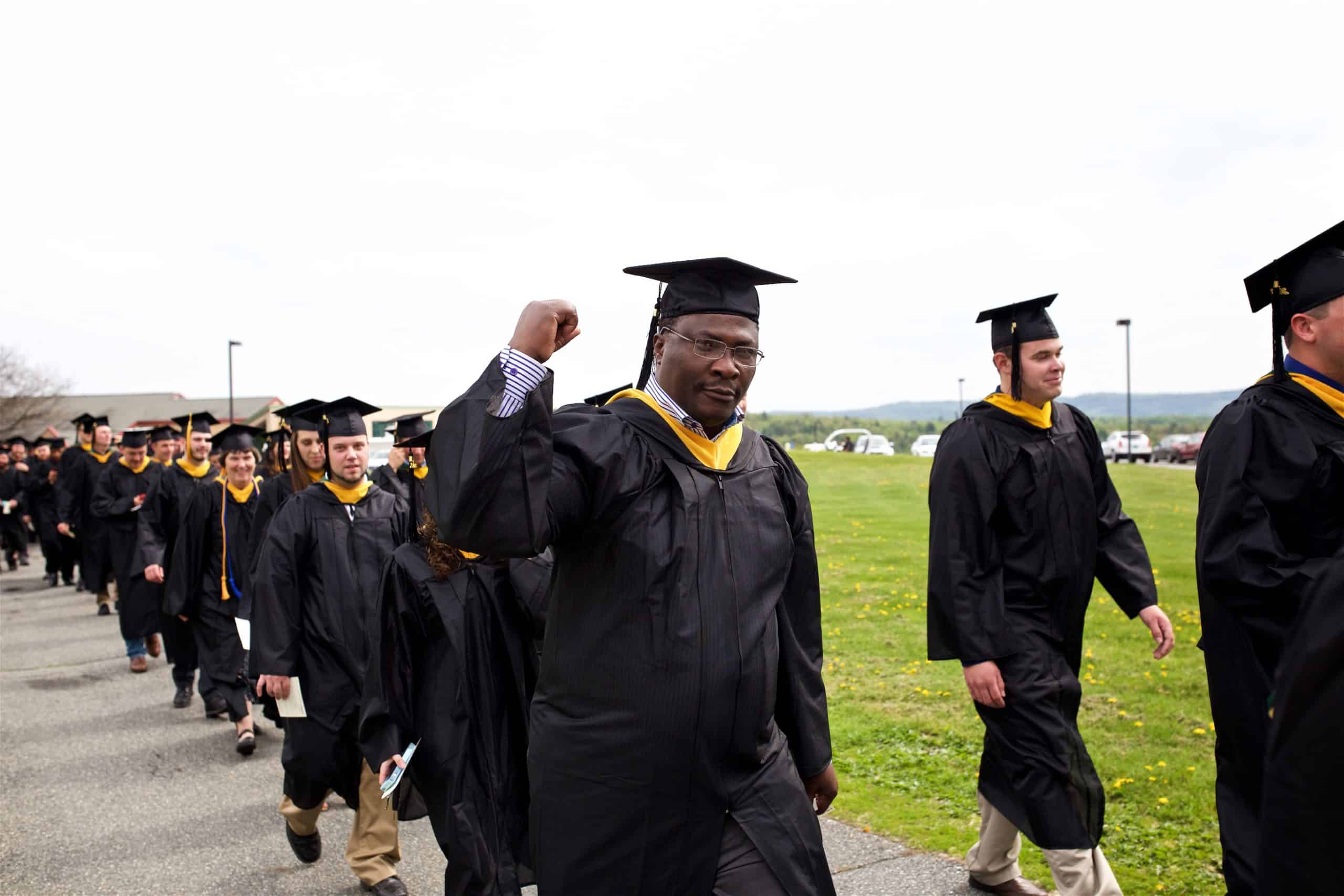 A proud graduate walking down the pathway with others.