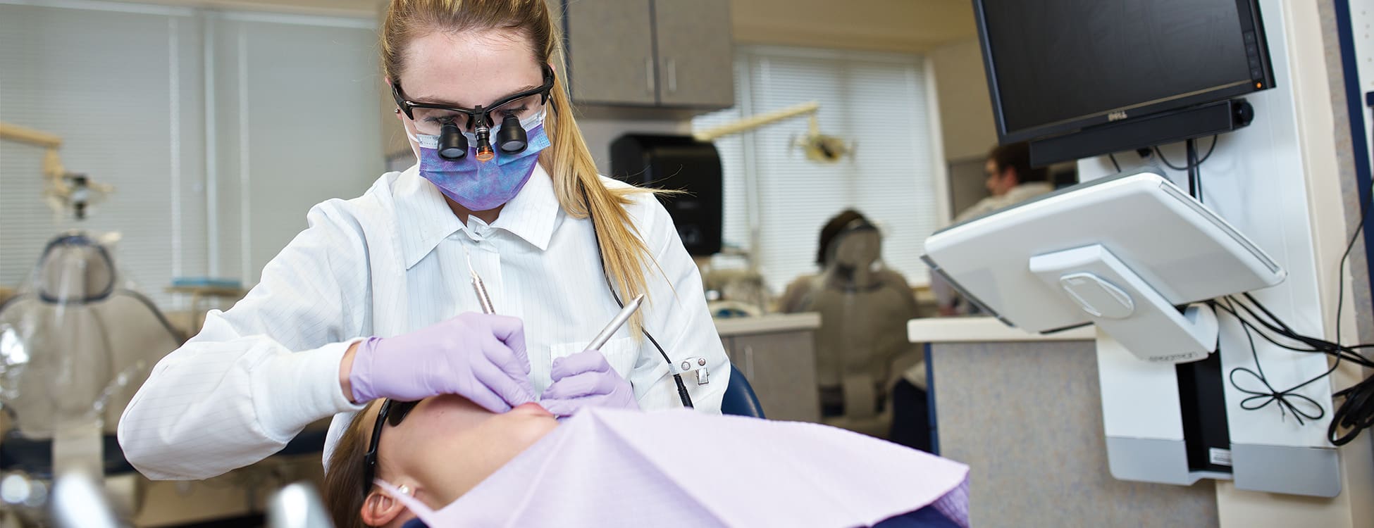 Vermont Tech dental hygiene students provides care to patient in chair wearing protective mask, gloves and eye wear, Williston campus, lab, hands on