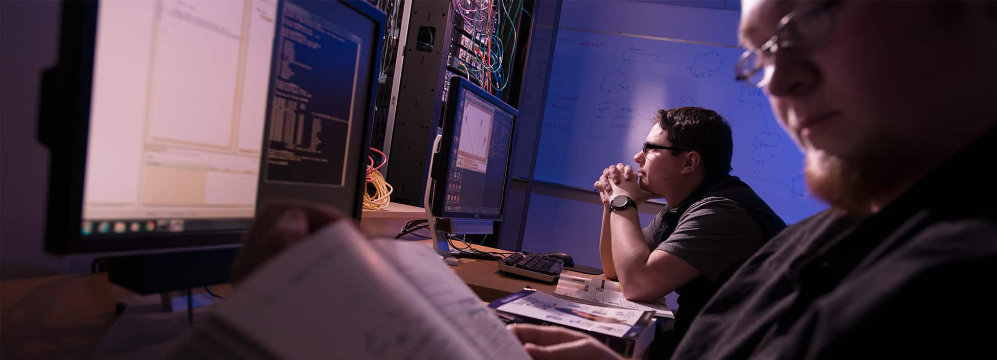 Two computer students work at computer screens with code in a dimly lit room