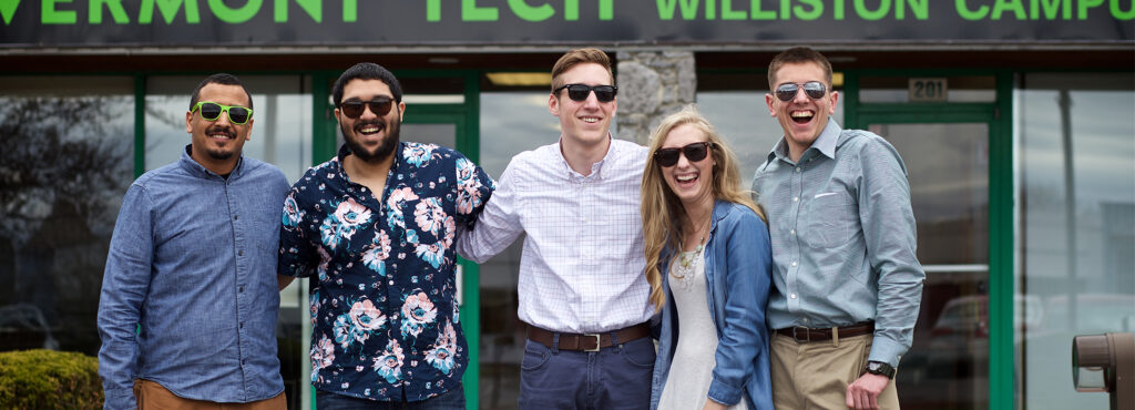 Five Vermont Tech students wearing sunglasses stand outside the Williston Campus Administration building