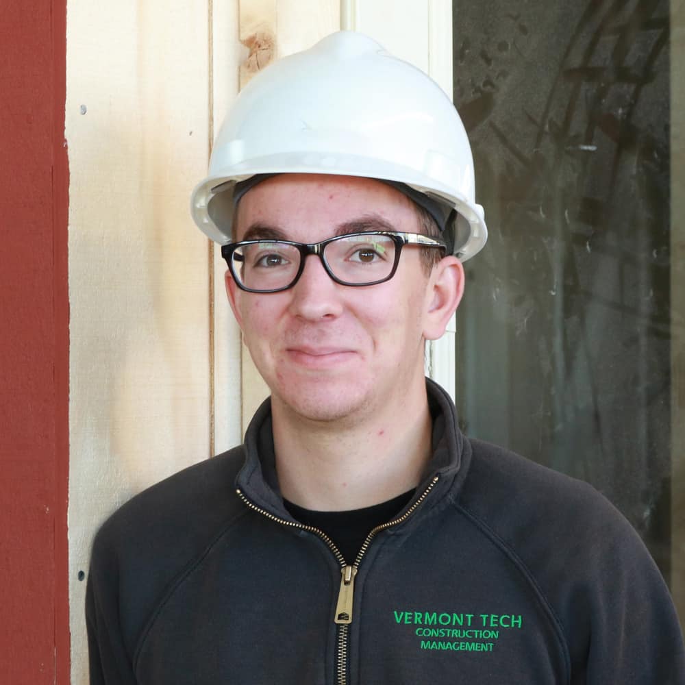 A male construction student wearing a hard hat smiles at the camera