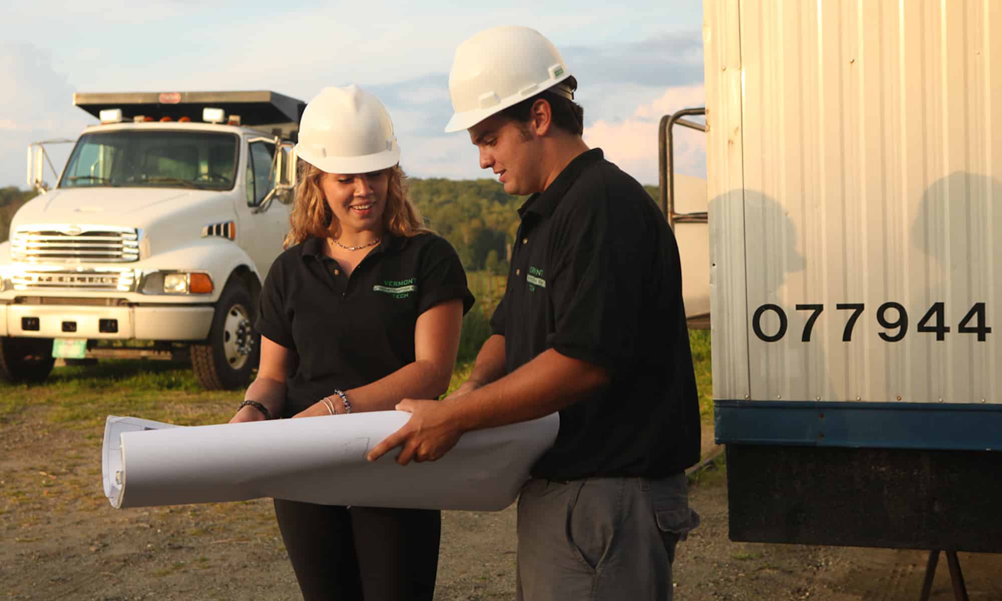 Two construction management students work on the job site and read construction plans together.