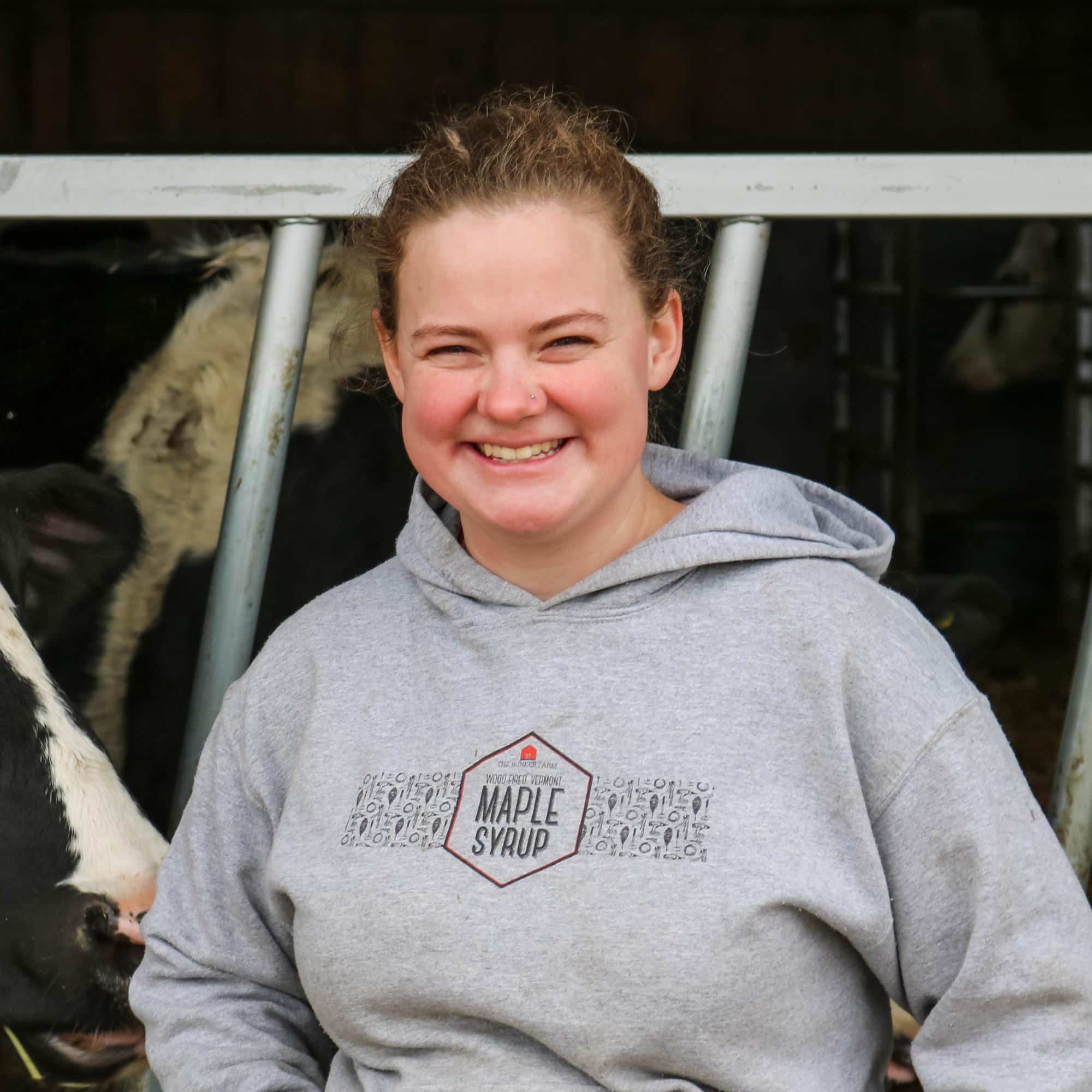 Louie Terrwilliger smiles at the camera with cows in the background at the barn