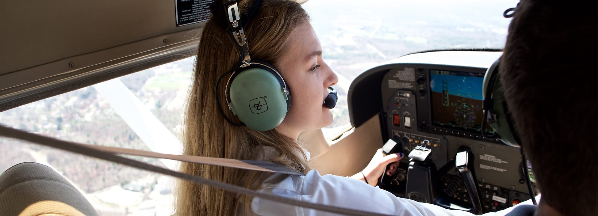 A female student adjusts controls on a plane dashboard as she soars above the Burlington area, professional pilot technology, pilot, STEM, hands on