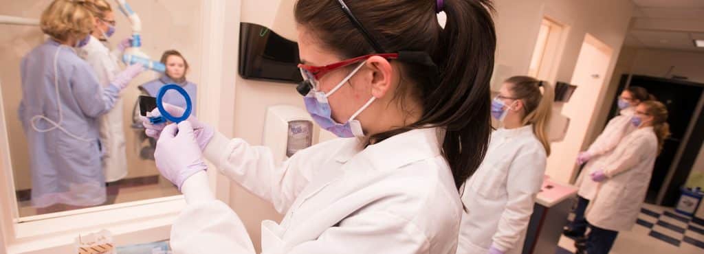 a dental student examines dental equipment before use in the lab, Williston campus, hands on