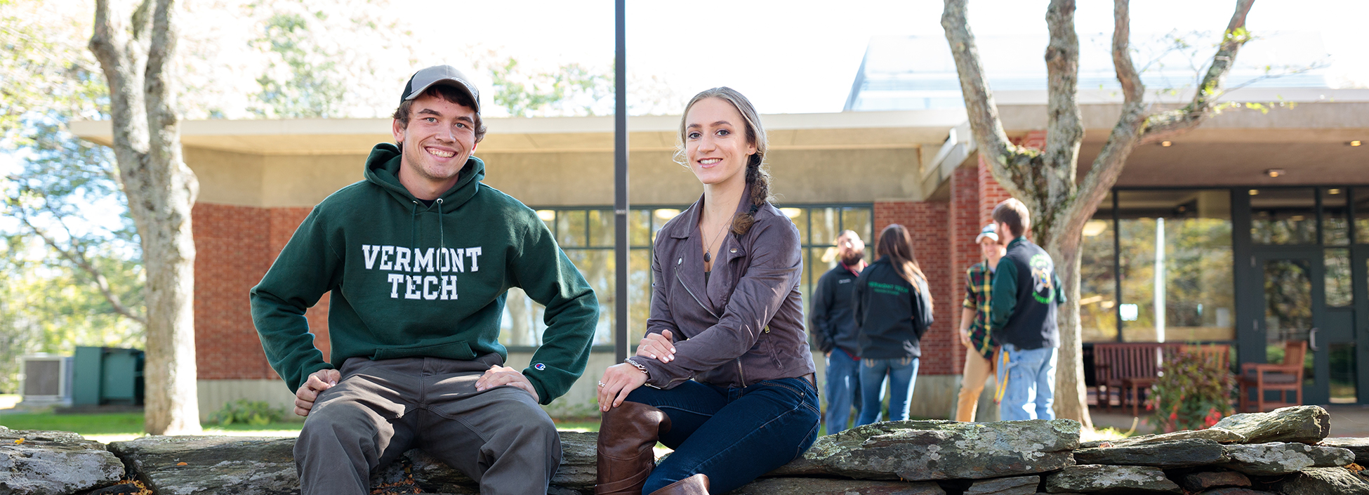 students smile and relax by the library on the stone wall, Randolph Center campus