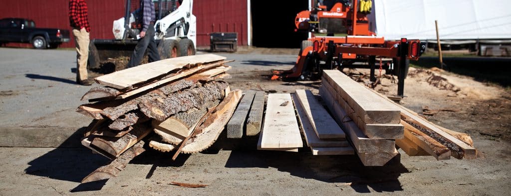 Piles of wood planks that have been planed from a tree lie on a pallet in front of saw, Randolph Center campus, forestry