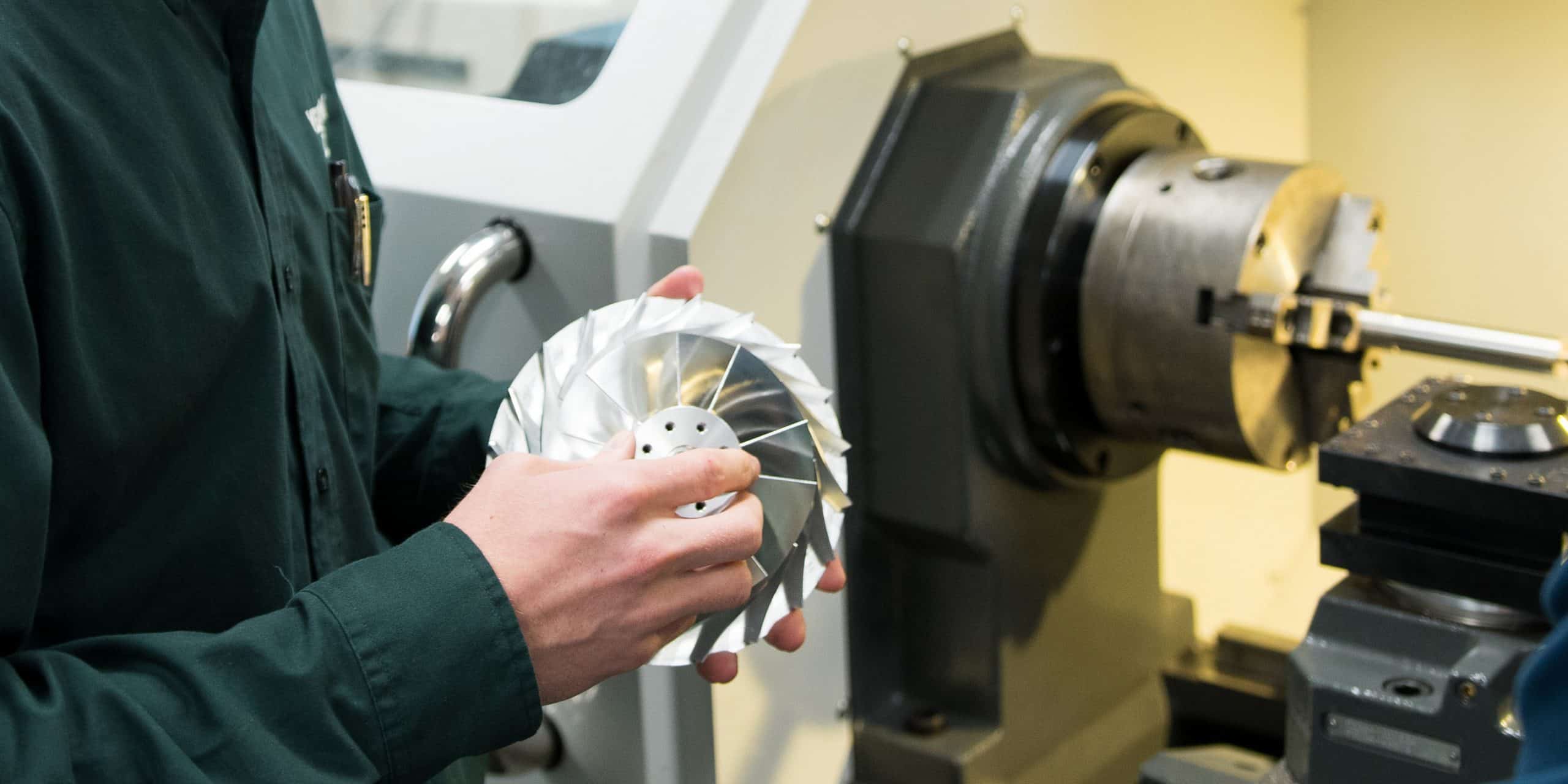 A machined part made from the lathe machine in the background, hand holding part