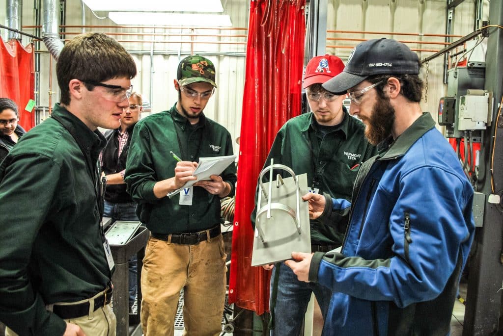 4 students look at a light fixture, hands on, senior project