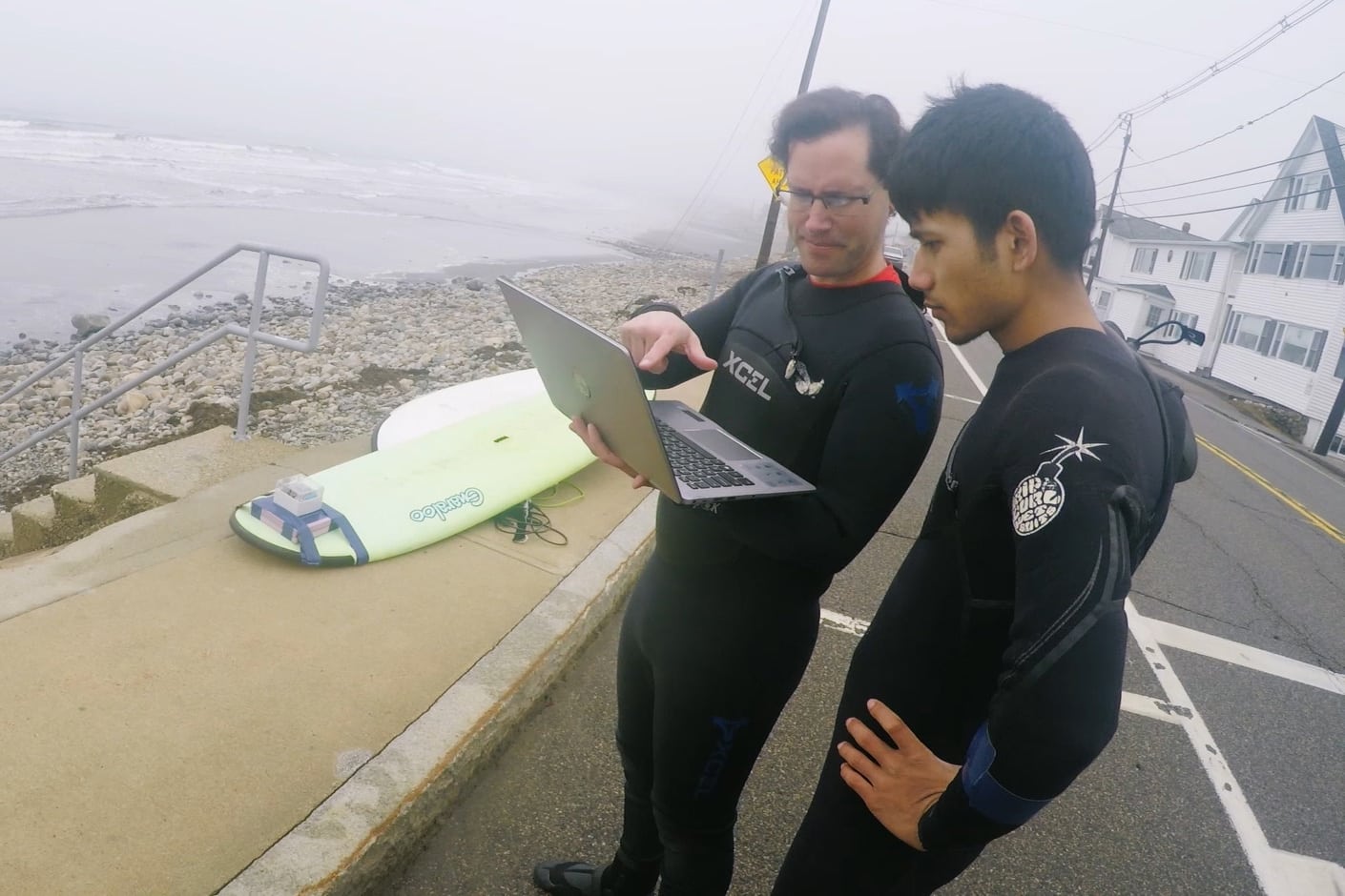 Josh and Puspa stand near the beach with a laptop, analyzing the data from their surfboard tracker, senior project