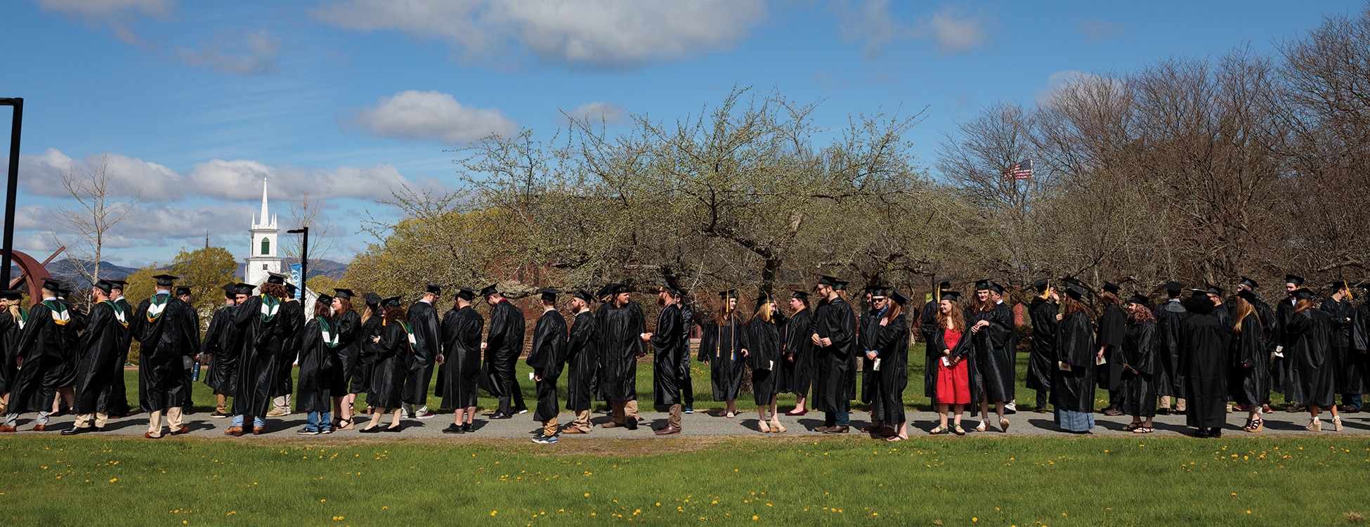 Vermont Tech graduates line up to process to the outdoor Commencement event on the Randolph Center campus in their caps and gowns on a sunny Vermont day.