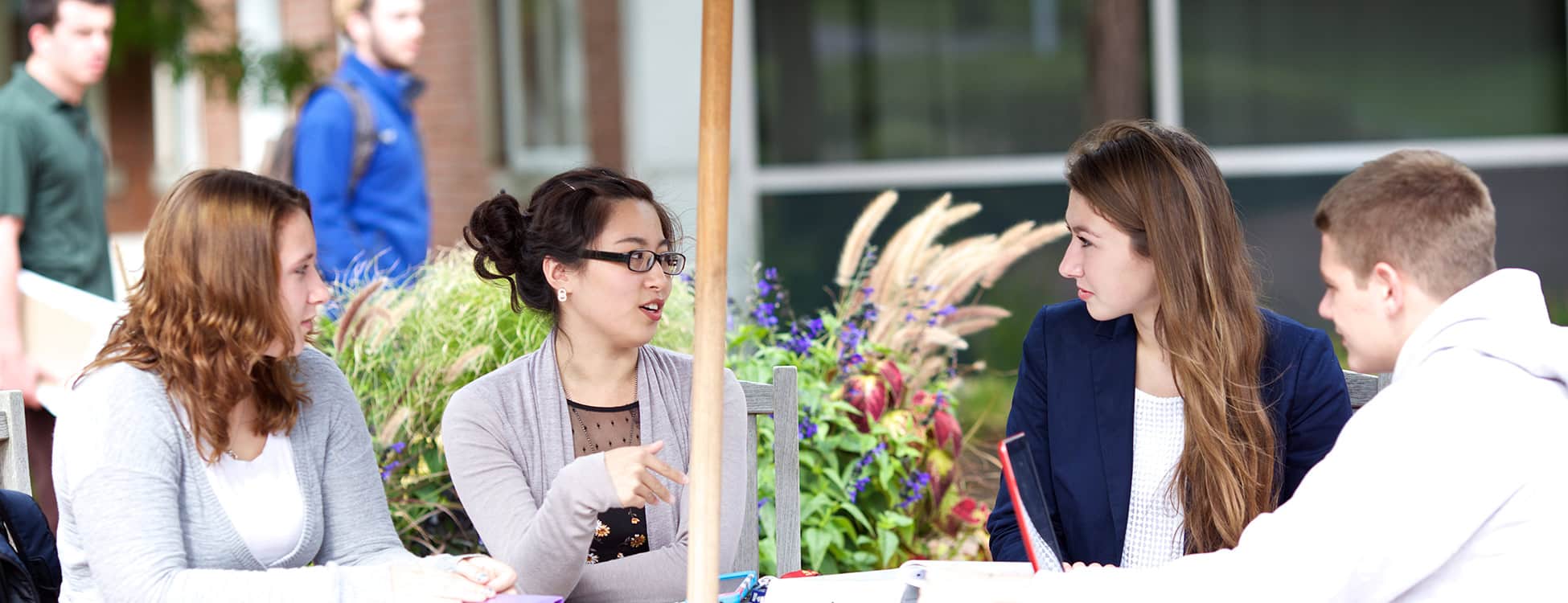 Students sit at table on patio, Randolph Center campus, chatting, smiling