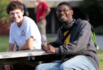 Male students, sitting outside on picnic table, ice cream, smiling