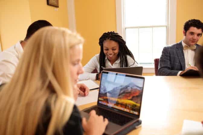 Business students sit around a yellow conference table working on laptops